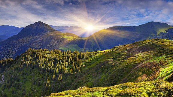 Sonne über begrünten Bergen